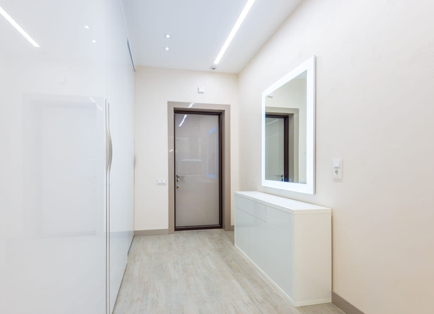A light hallway with a tall closet and a white cabinet under an illuminated mirror