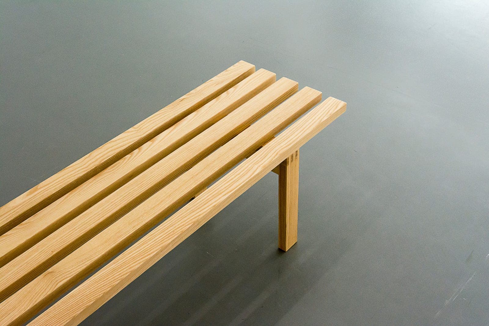 A simple wooden bench in a minimalist room on a gray floor