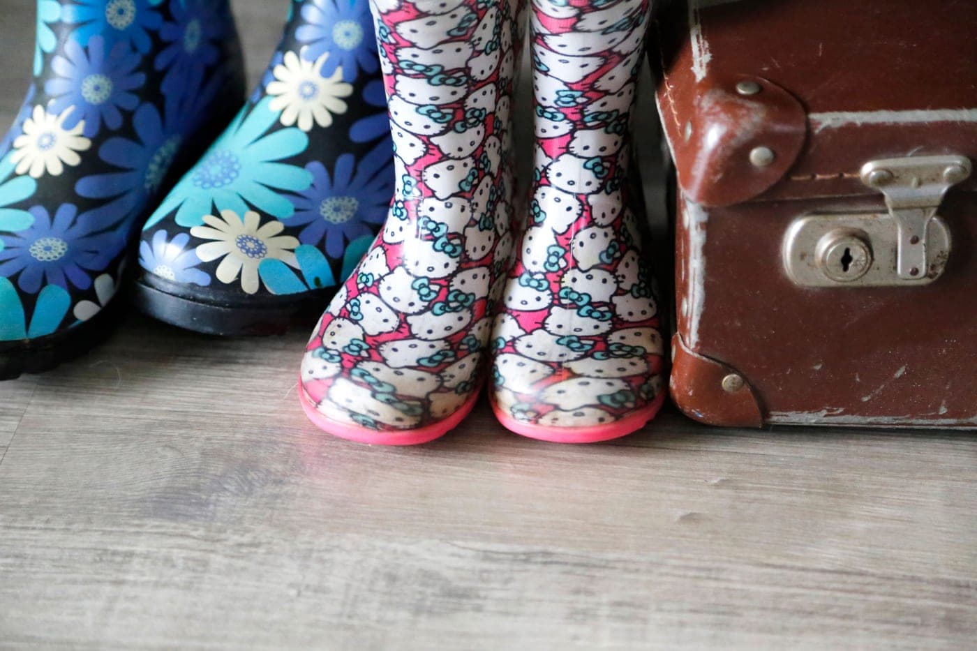 Patterned rain boots and a vintage suitcase on a wooden floor