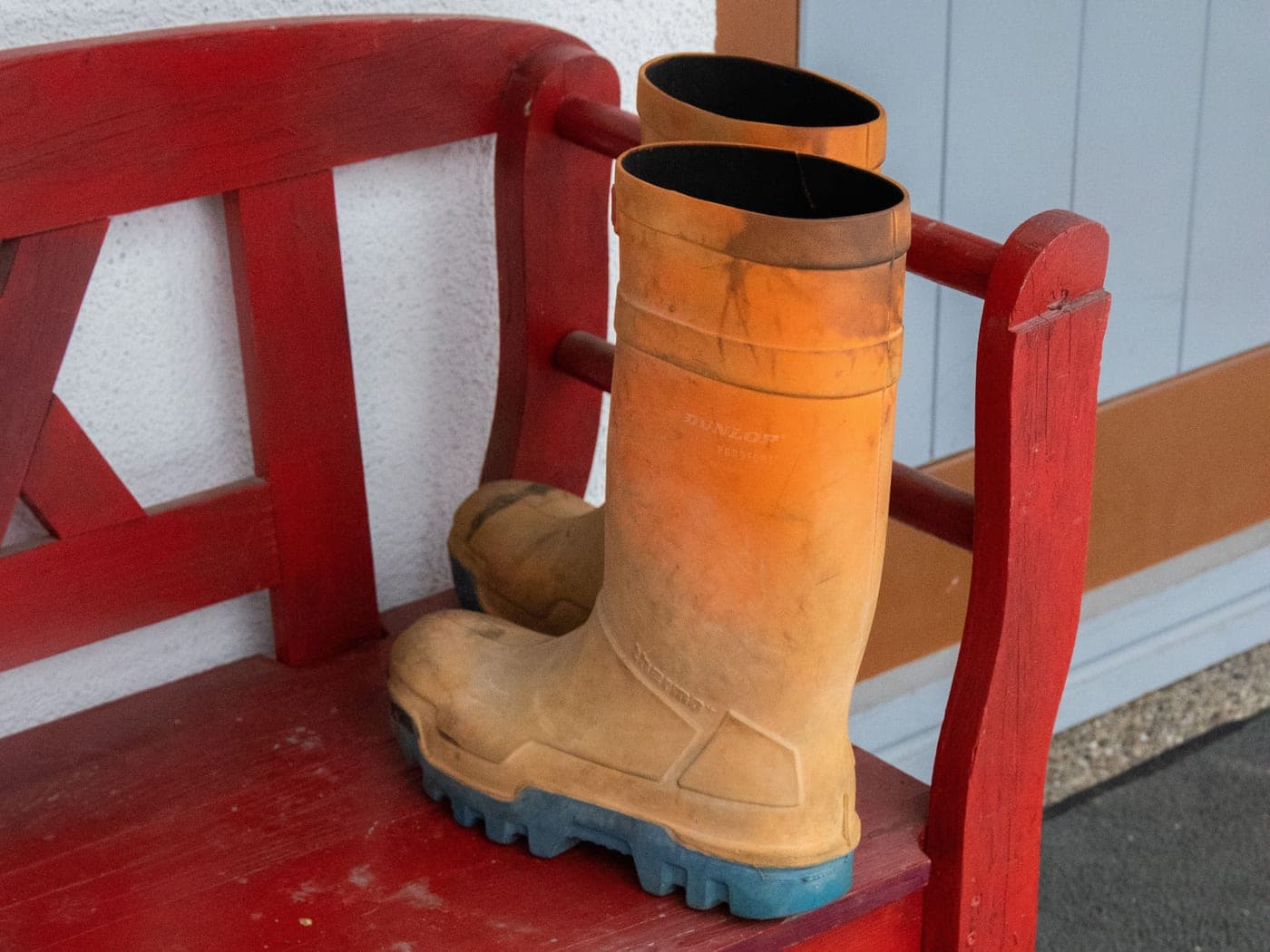 A pair of rubber boots standing on a bench beside a doorway