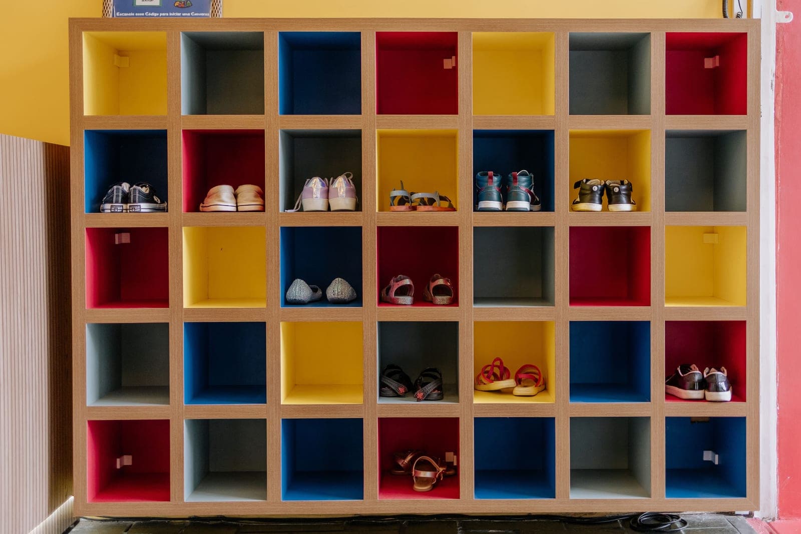 A cubical shoe cabinet with multicolored boxes holding various footwear