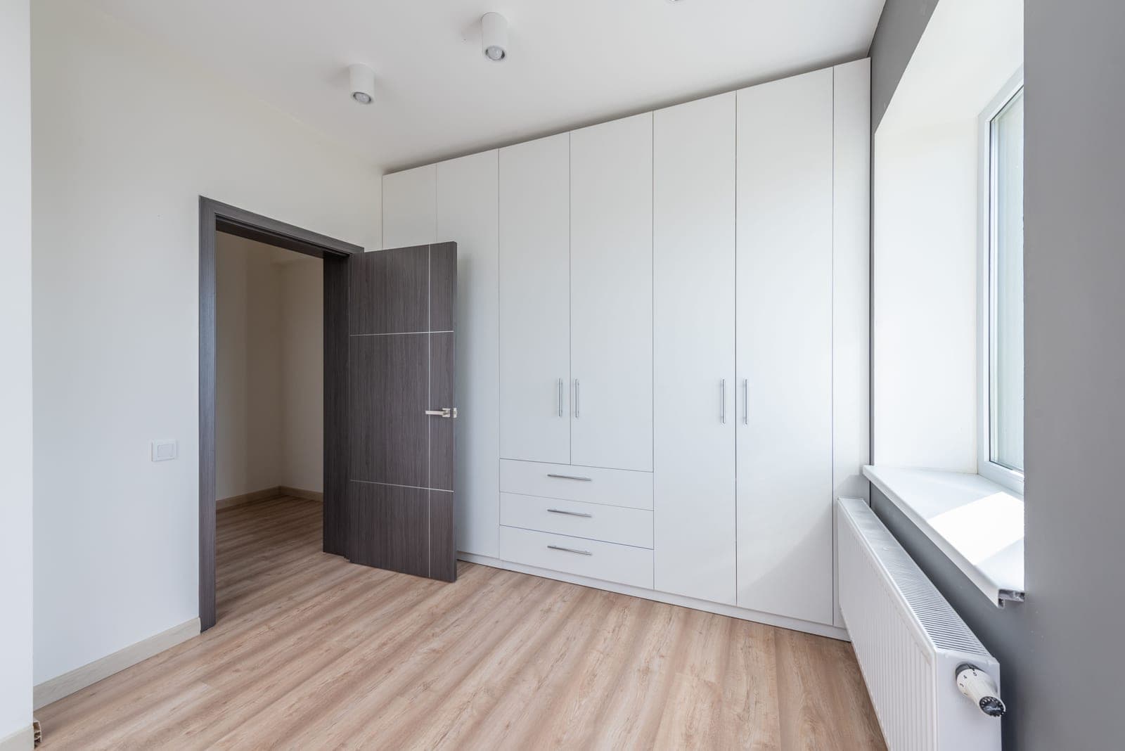 A bright empty room with sleek white cabinets and wooden flooring