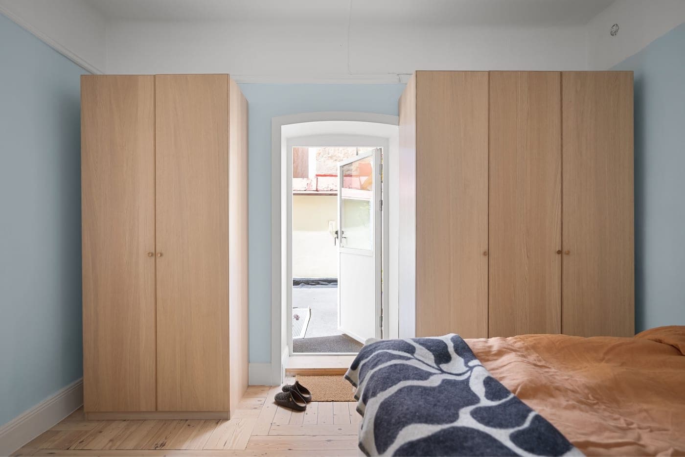 A bedroom with wooden wardrobes and a low cabinet beside the bed