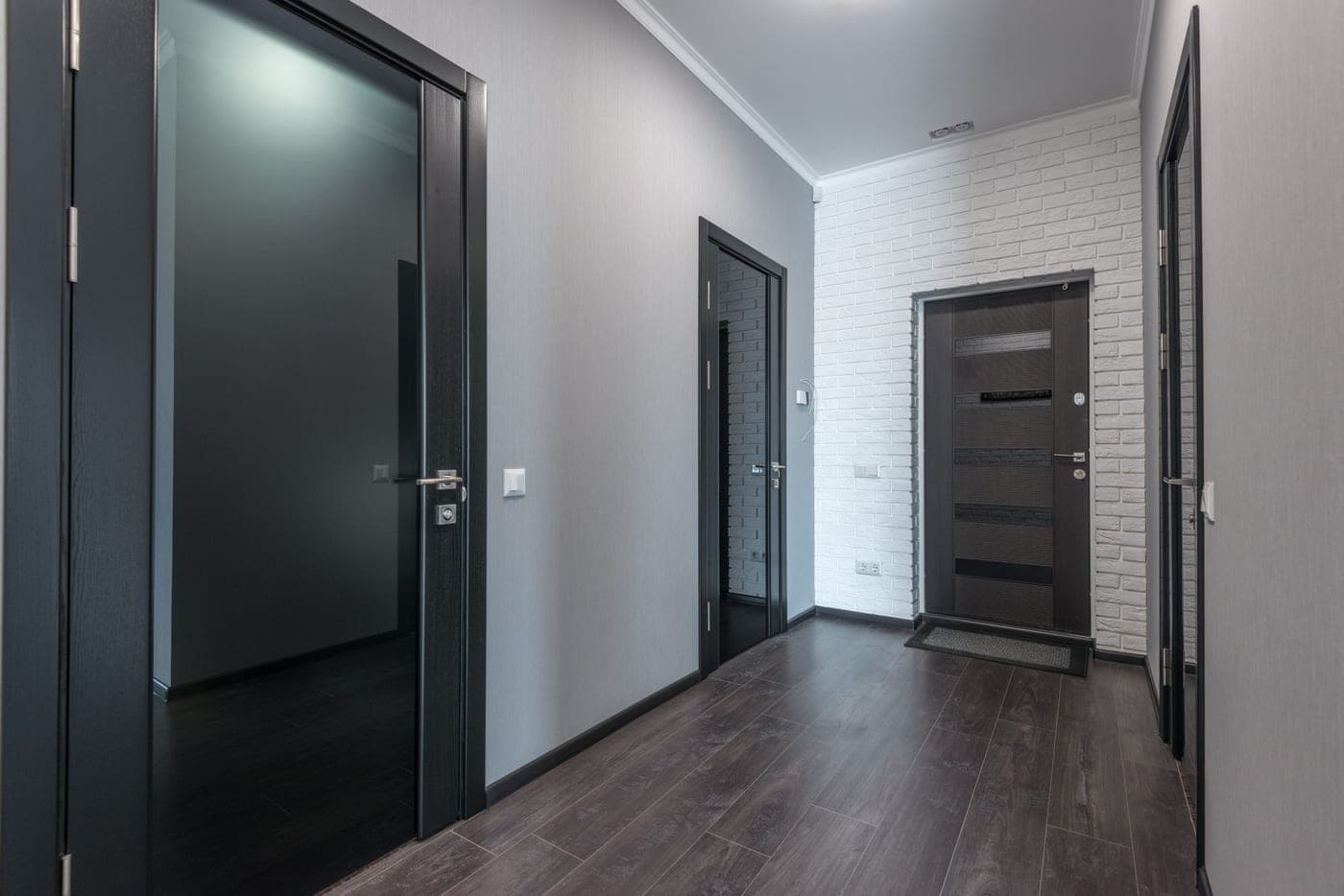 An empty corridor with laminate flooring, gray walls and black doors