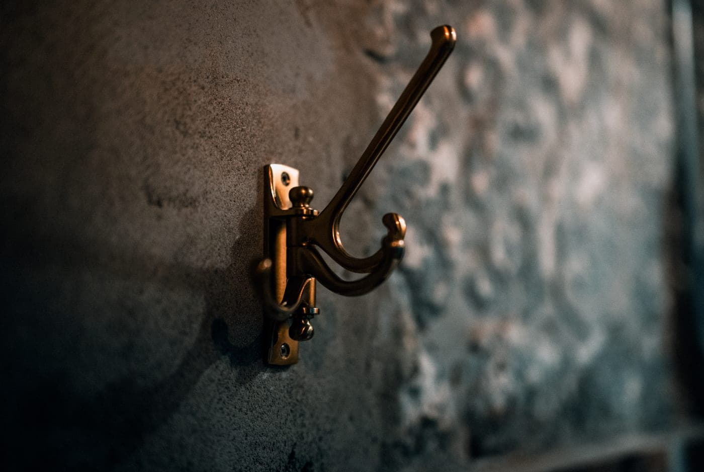 A brass coat hook mounted on a textured wall