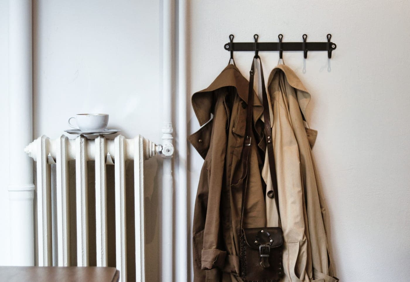 Coats and a bag hanging from a row of wall hooks in a hallway