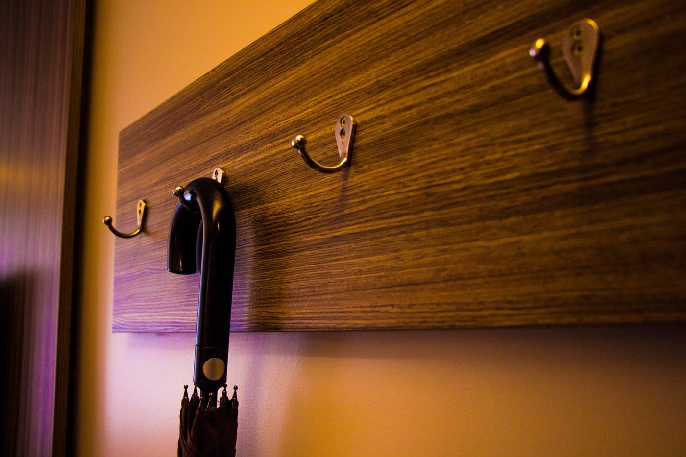 A wooden hook board on an indoor wall with an umbrella hanging from it