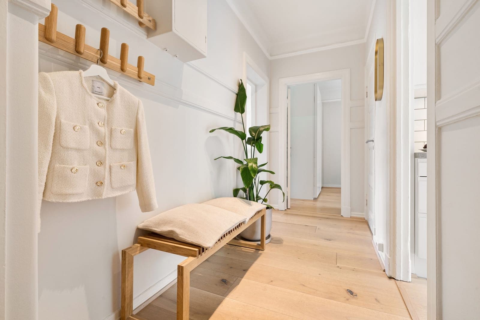 A bright entryway with a wooden bench against the wall and coats hanging above it