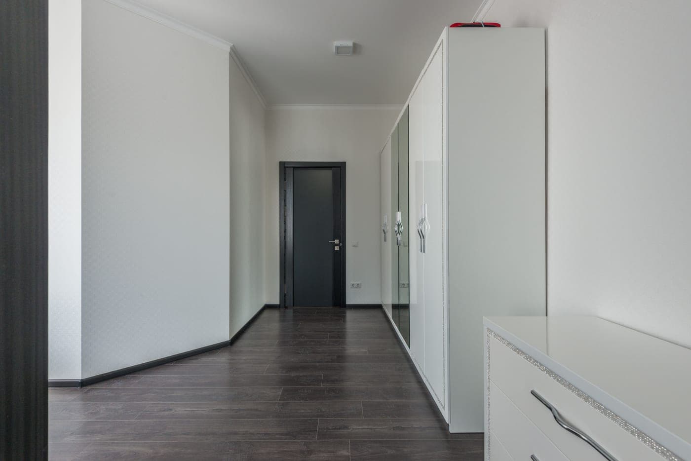An empty hallway with a wooden floor, white walls and a black entrance door