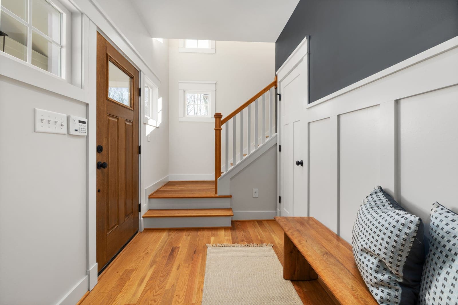 A bright entryway with wooden flooring, a bench and natural light