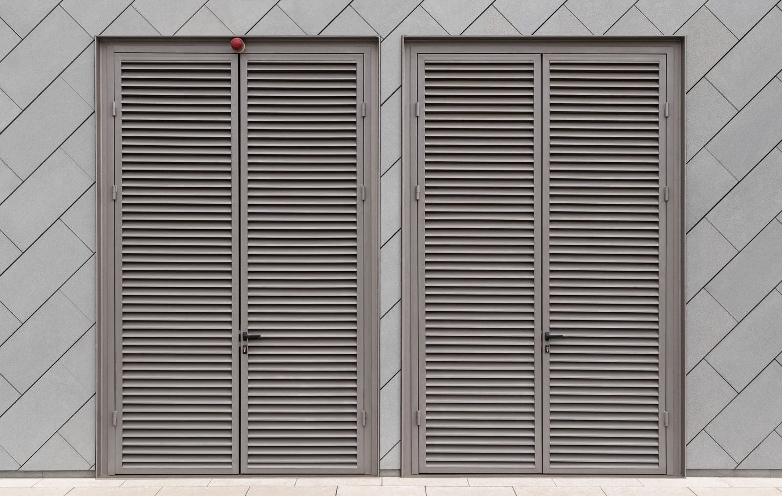 A pair of minimalist grey louvered doors set into a patterned concrete wall